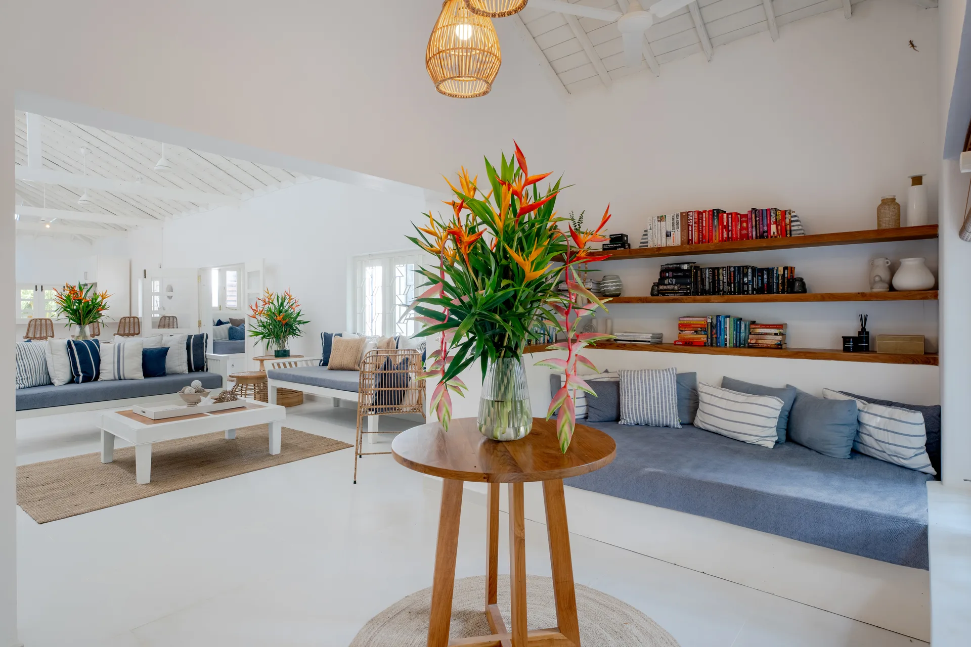 Open plan white living room with book wall and tropical flowers