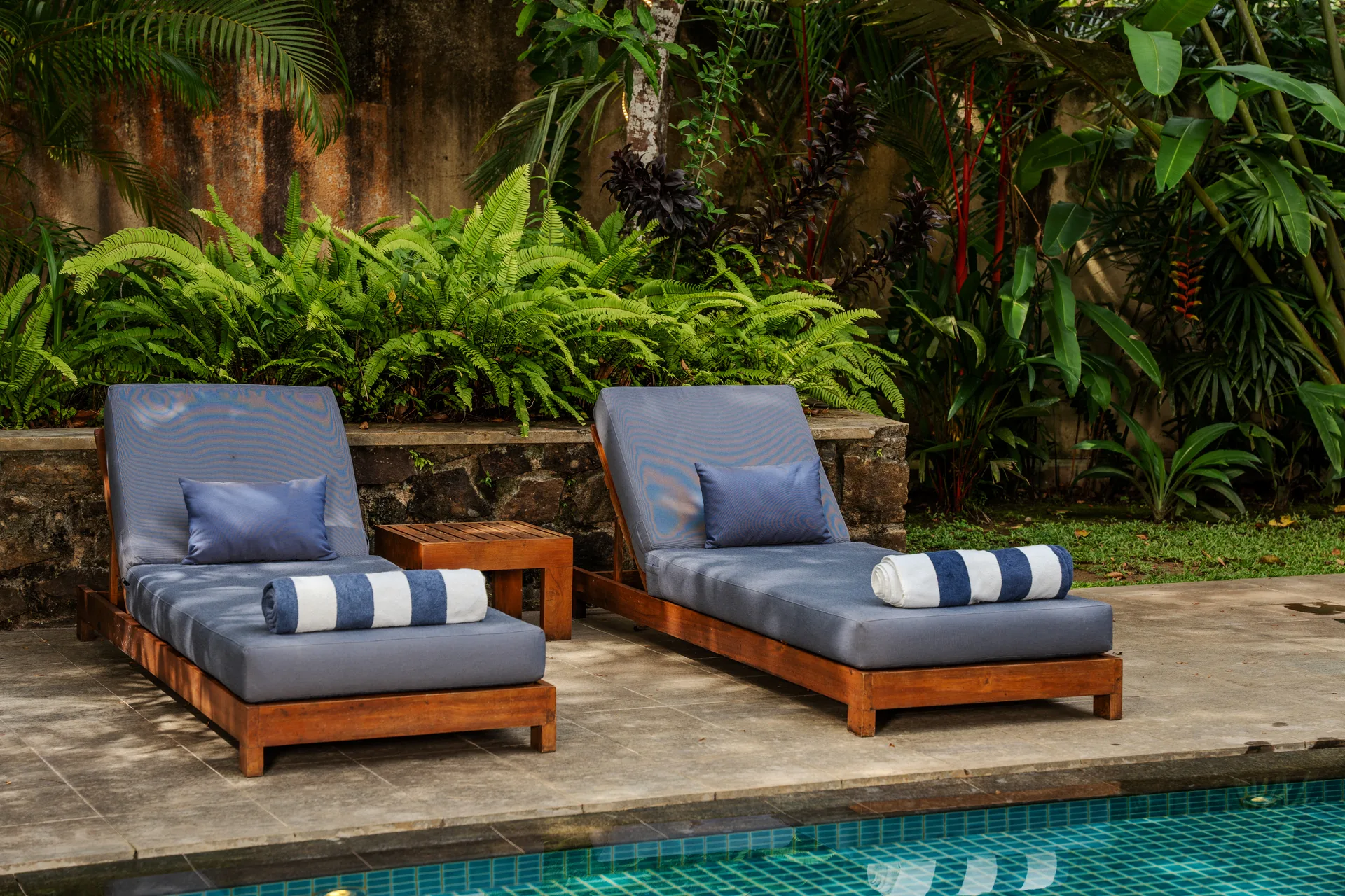 Custom teak sun loungers with striped towels by the pool